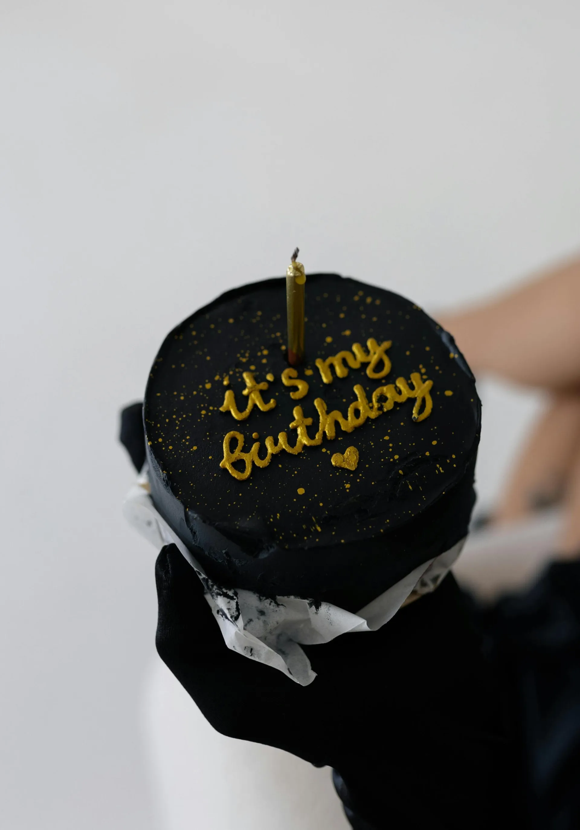 Stylish black cake with golden 'It's my birthday' icing and candle.