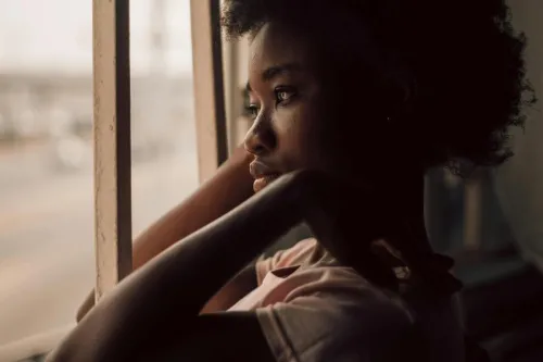 A young woman with afro hairstyle gazing contemplatively outside through a window.