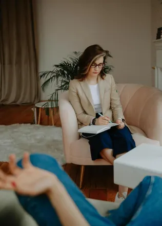 Female therapist writing notes during a counseling session, focusing on mental health.