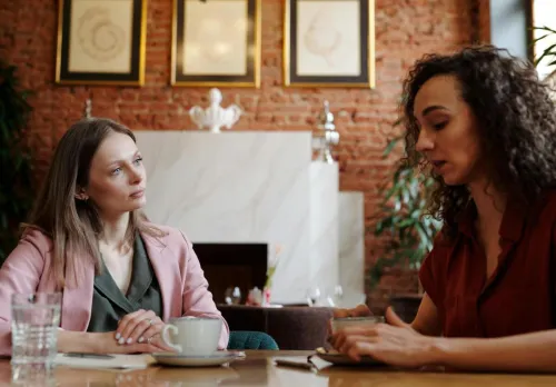 Two women engaged in serious discussion over coffee in a cozy indoor café setting.