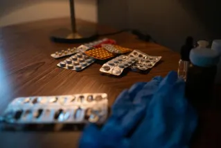 Close-up of various medication blister packs and gloves on a wooden table, signifying health and recovery.