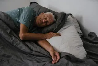 Elderly man resting comfortably in bed, serene indoor atmosphere.