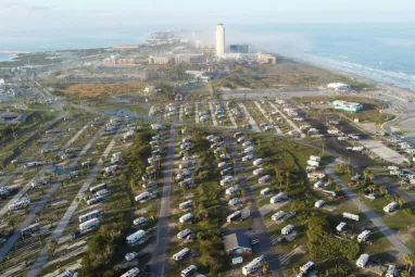 Aerial view of a coastal RV park near the ocean, showcasing numerous caravans and nearby resort buildings.