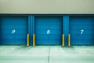 Three blue shutter doors numbered 9, 8, and 7 with yellow barriers in urban environment.