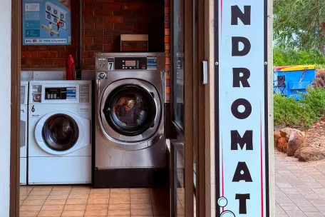 Entrance of a laundromat with neon open sign and washing machines visible.