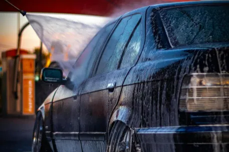 A car wash in progress with soap and water on a car under a vibrant sky.