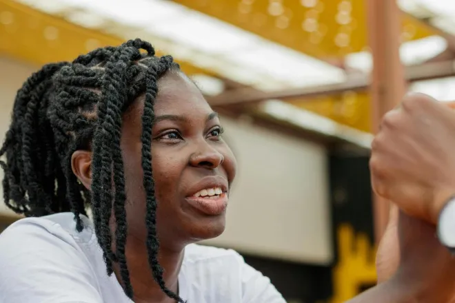 Close-up of a smiling woman with braided hair in an outdoor setting in Accra, Ghana.