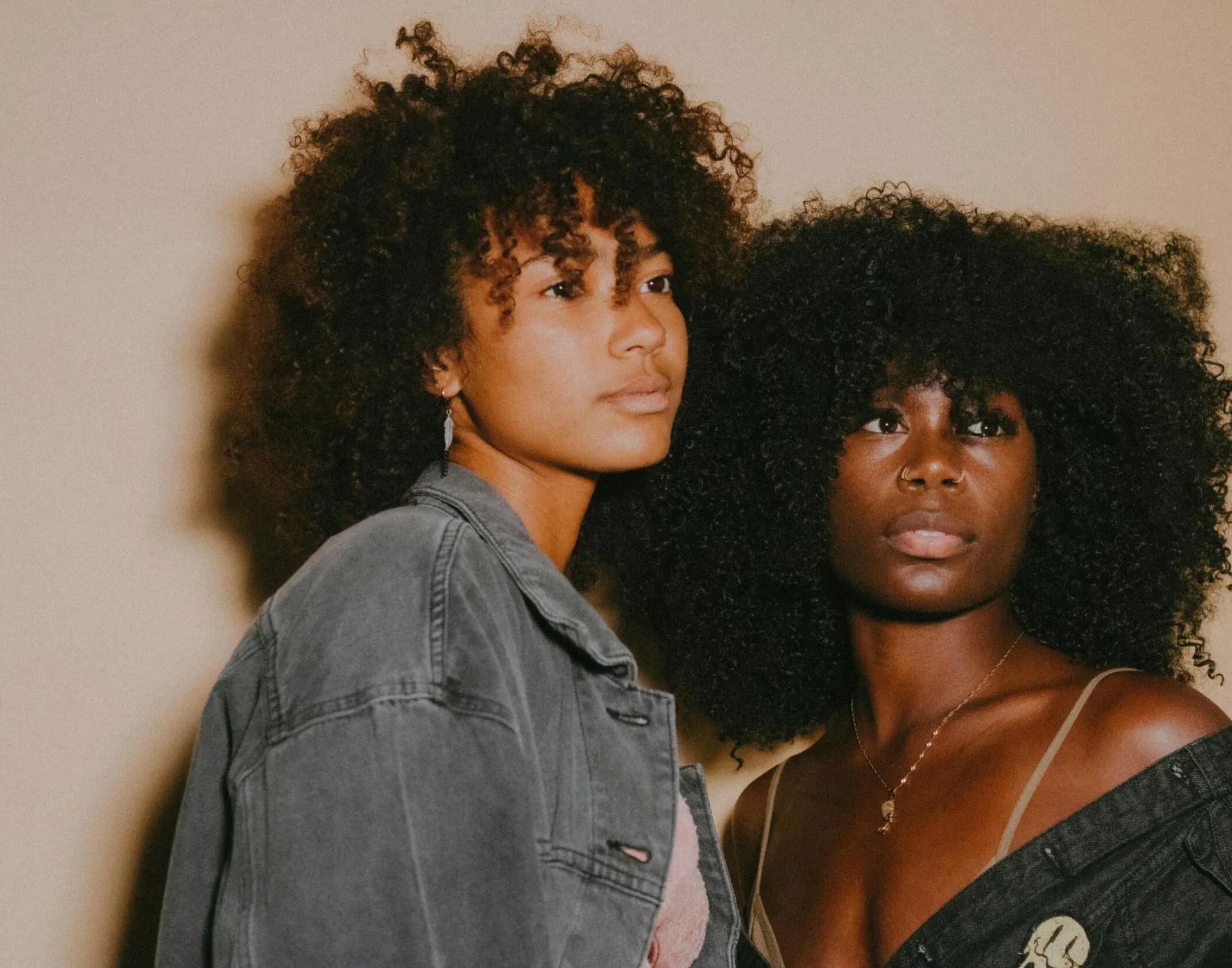 Captivating studio portrait featuring two young women with afro hair in denim jackets.