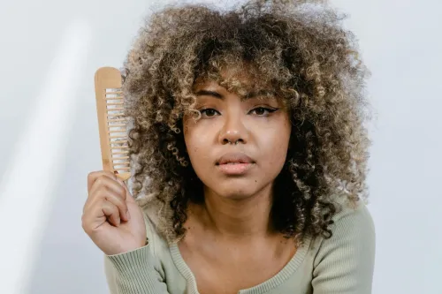 Portrait of a woman with natural afro hair holding a wooden comb, emphasizing beauty routines.