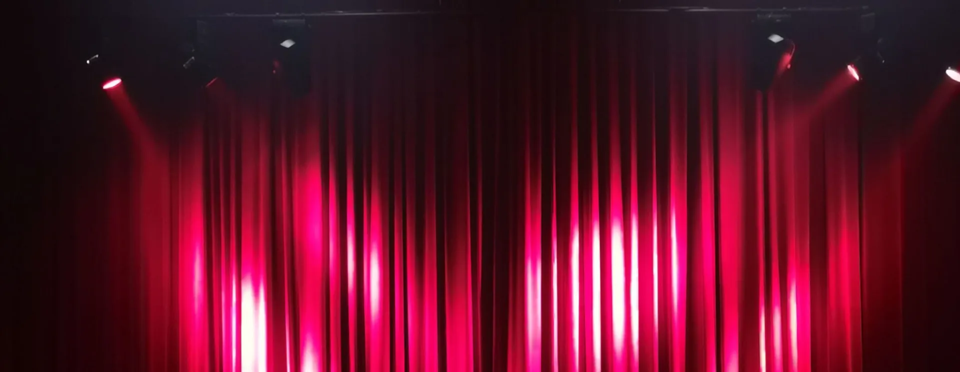 A dramatic scene of red curtains in a theater with empty seats, ready for a performance.