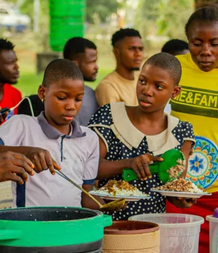 People gathered outdoors sharing and preparing a traditional meal. Vibrant cultural scene.