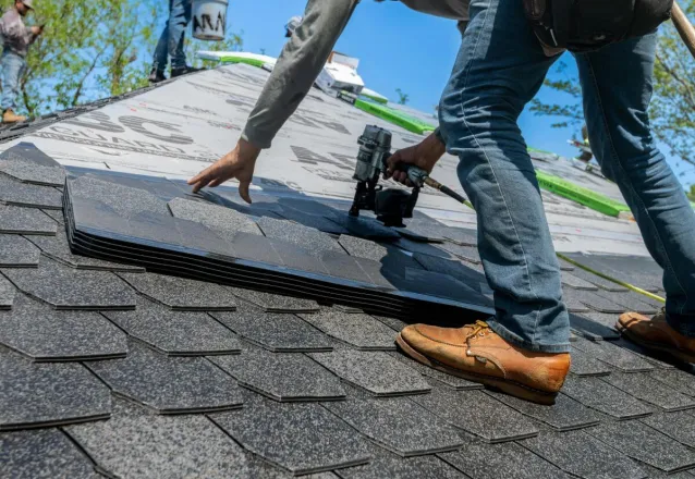 Roofer using nail gun for shingle installation on residential roof.
