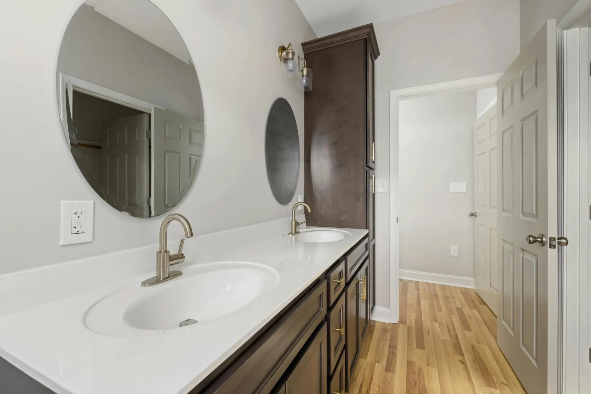 A stylish bathroom interior featuring dual round mirrors, a double sink vanity, and wooden flooring.