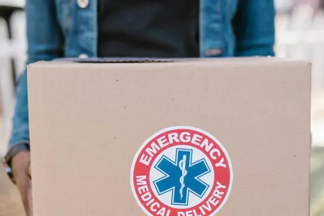 Person holding a box labeled 'Emergency Medical Delivery,' representing urgent healthcare logistics.