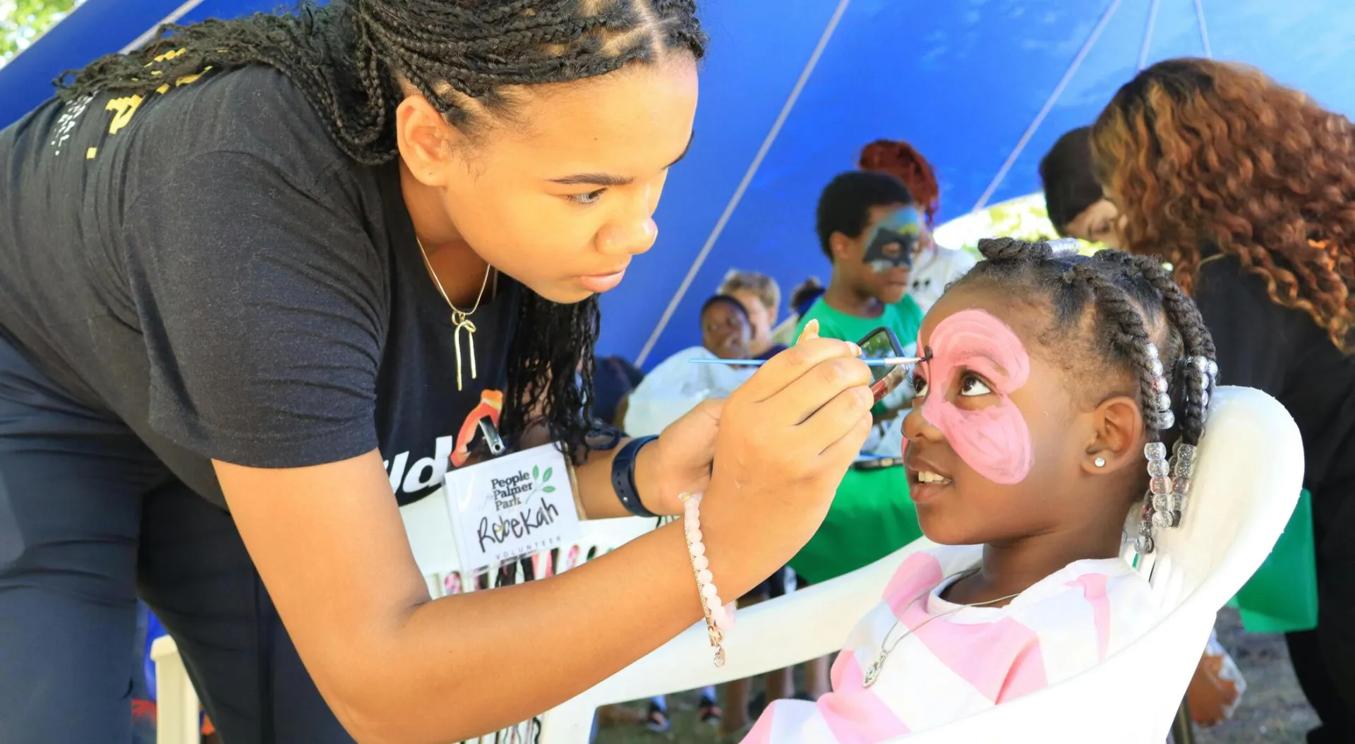 A young woman paints a child's face at an outdoor festival, enhancing community joy and creativity.