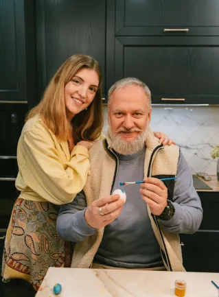 Father and daughter joyfully painting Easter eggs together in a cozy kitchen setting.