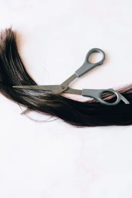Scissors cutting a lock of brown hair on a white background, symbolizing hair styling or cutting.