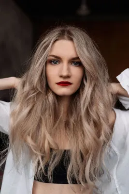 Elegant portrait of a woman with long wavy blond hair and red lipstick, showcasing natural beauty and style.