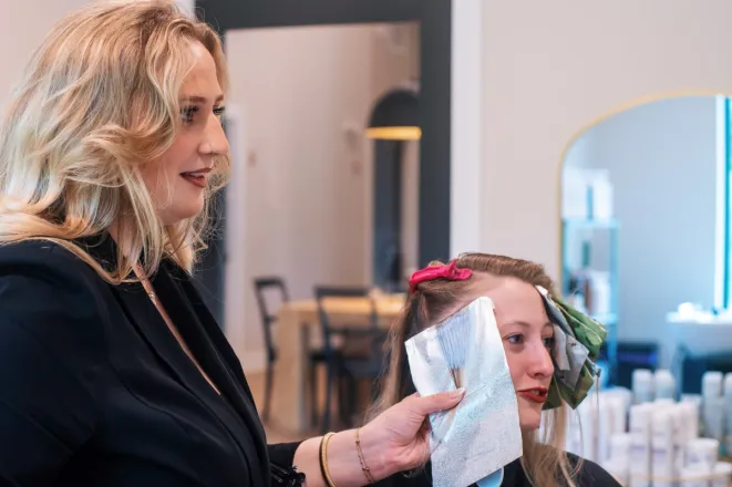 A hairdresser applies dye in a salon, capturing a professional hair treatment in stylish black and white.