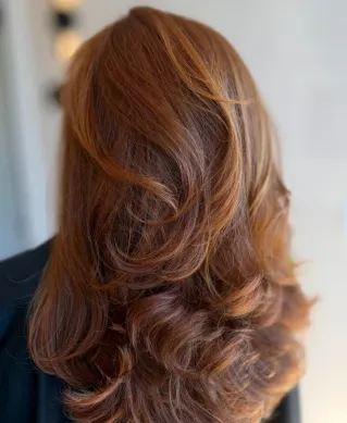 Close-up of red hair being trimmed with scissors and comb on green background.