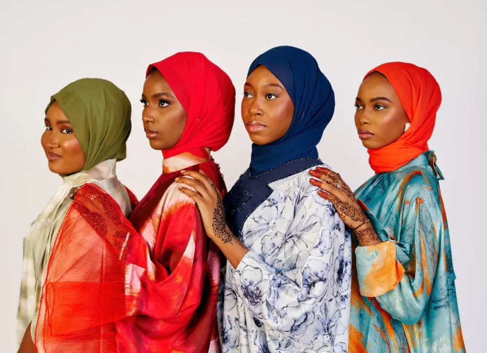 Four women wearing colorful hijabs posing confidently indoors.
