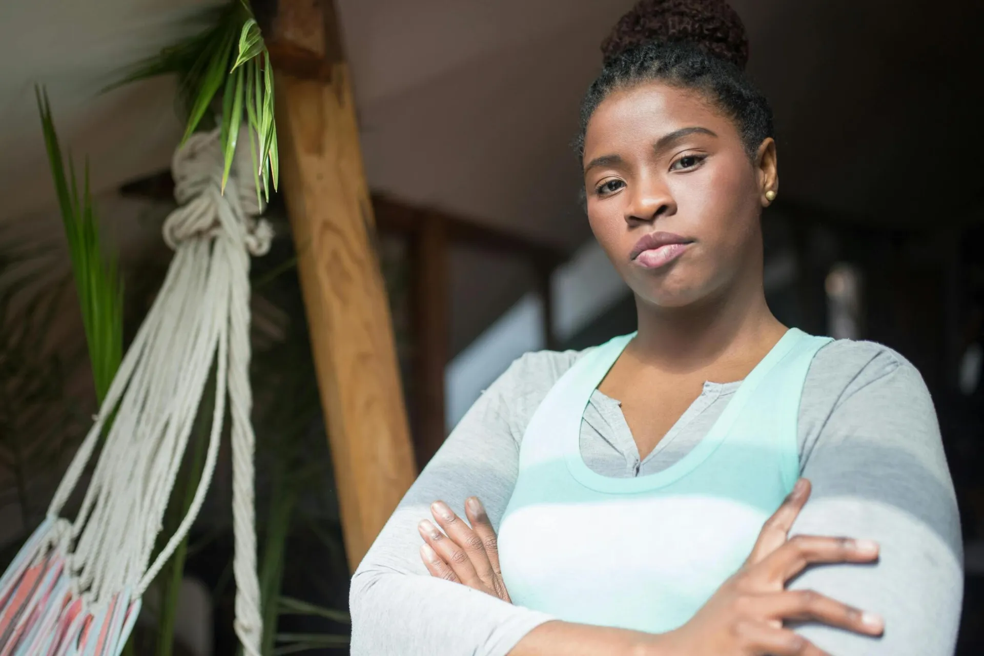 Portrait of a confident woman standing indoors with arms crossed beside a hammock.