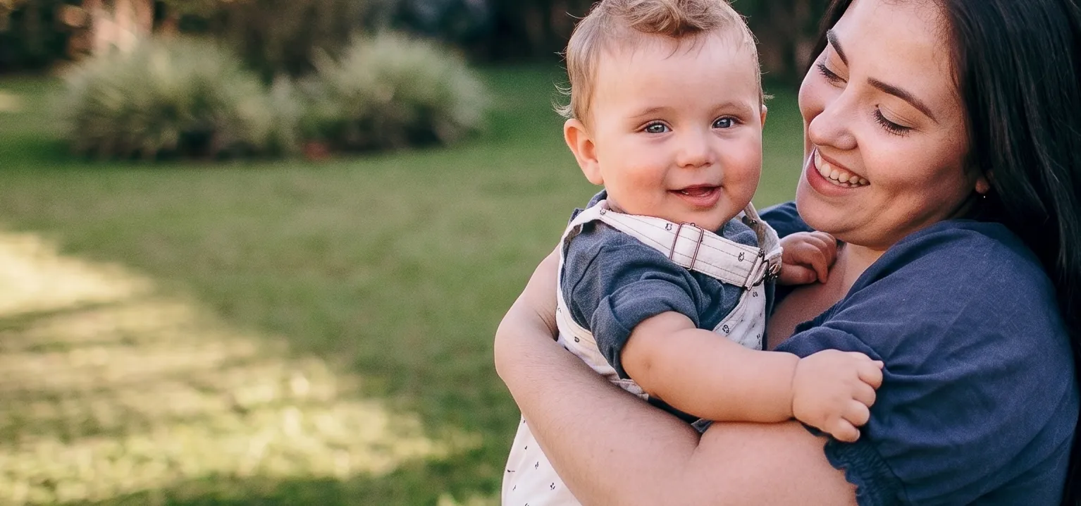 Smiling parents holding their baby in an outdoor garden setting, spending quality time together.