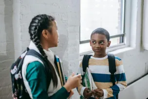 Content multiracial pupils with copybooks and backpacks standing in school corridor and having conversation