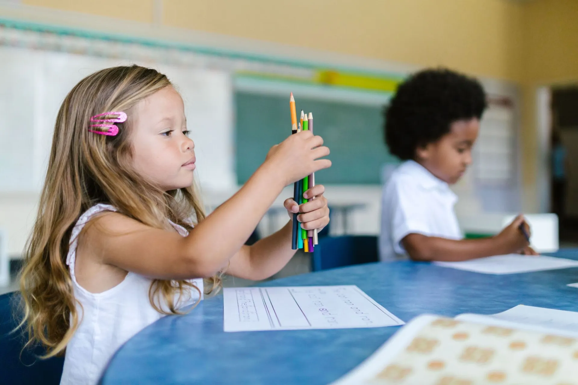 Two children focused on classroom learning with colored pencils and paper.