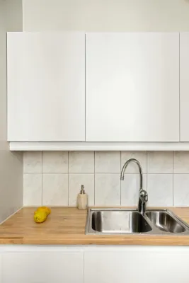 Elegant minimalist kitchen with stainless steel sink, lemon, and white cabinets.