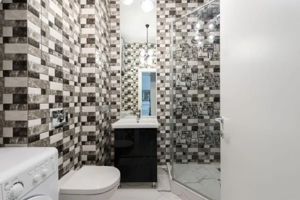 Interior of bright washroom with washing machine near toilet next to shower and sink with tap