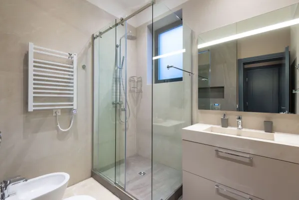 Shower cabin with glass walls near mirror hanging on wall above sink in modern minimalist styled bathroom