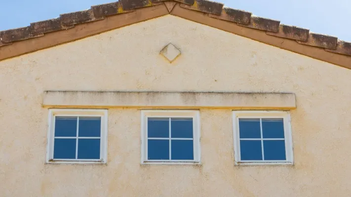 Close-up view of a house facade featuring three evenly spaced glass windows under a triangular roof.