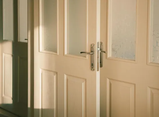 Elegant wooden doors with frosted glass panels softly illuminated by streaming sunlight.