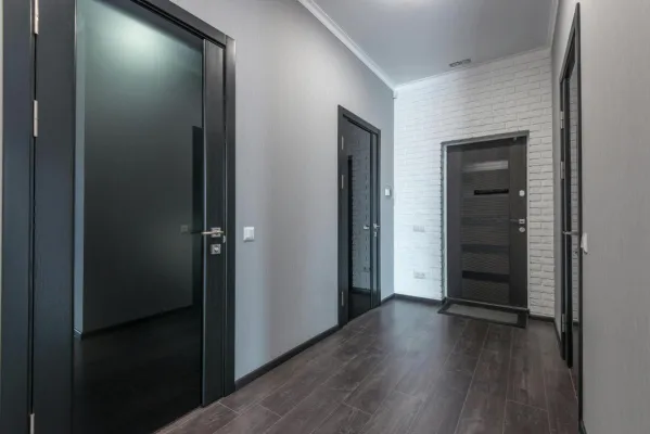 Interior of empty spacious corridor with laminate floor and black doors with glass parts and white ceiling and gray painted walls