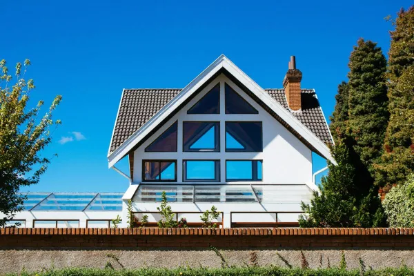 Contemporary A-frame house with large glass windows on a sunny day, surrounded by greenery.