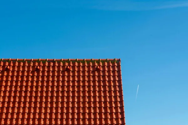 Minimalist photo of a red tiled rooftop contrasting against a clear blue sky.