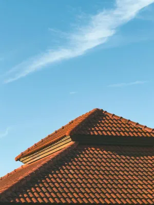 Red tiled roof against a clear blue sky with wispy clouds, highlighting architectural design.