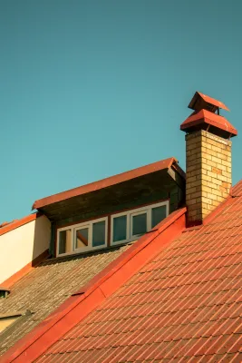 A rooftop featuring a sunlit brick chimney and skylight under a clear blue sky.