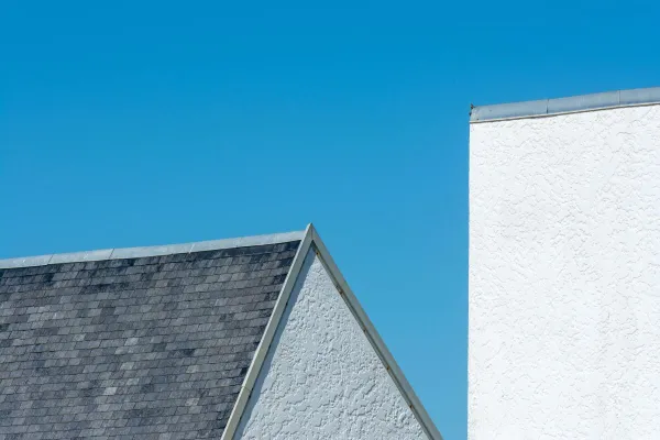 A minimalist view of triangular rooflines and white walls beneath a clear blue sky.