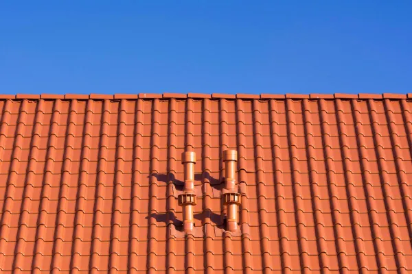 Vivid red clay rooftop with patterns and vents beneath a clear blue sky, ideal for architecture themes.