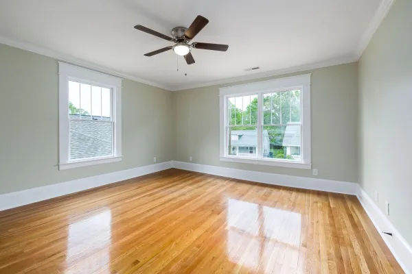 Bright empty room with wooden floors, large windows, and a ceiling fan.