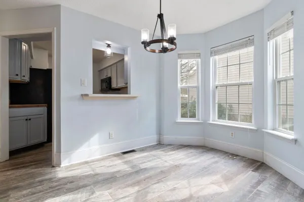 Sunlit empty room featuring a modern chandelier and wooden floors, ideal for home staging.