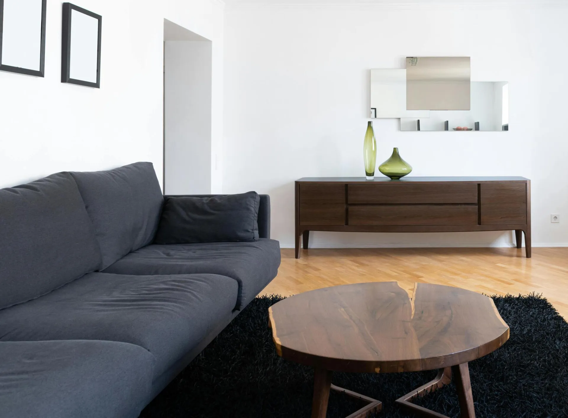 Interior of modern light home with couch near wooden table on carpet near cabinets with vases and TV