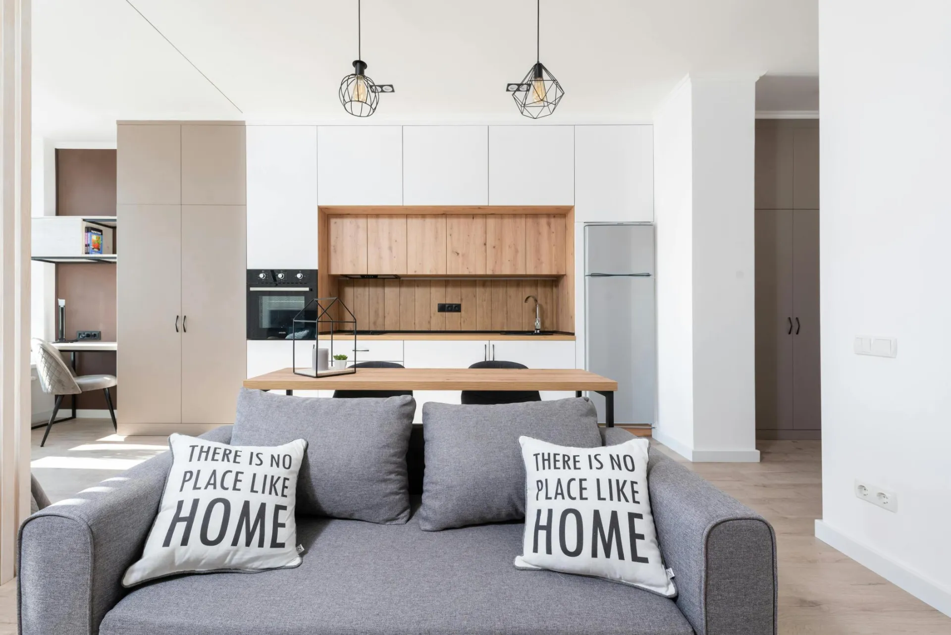 House interior with couch with pillows near table and open kitchen with cabinets and oven with fridge