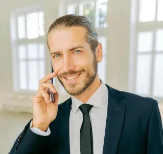 Smiling businessman in a suit making a phone call in a bright office setting.