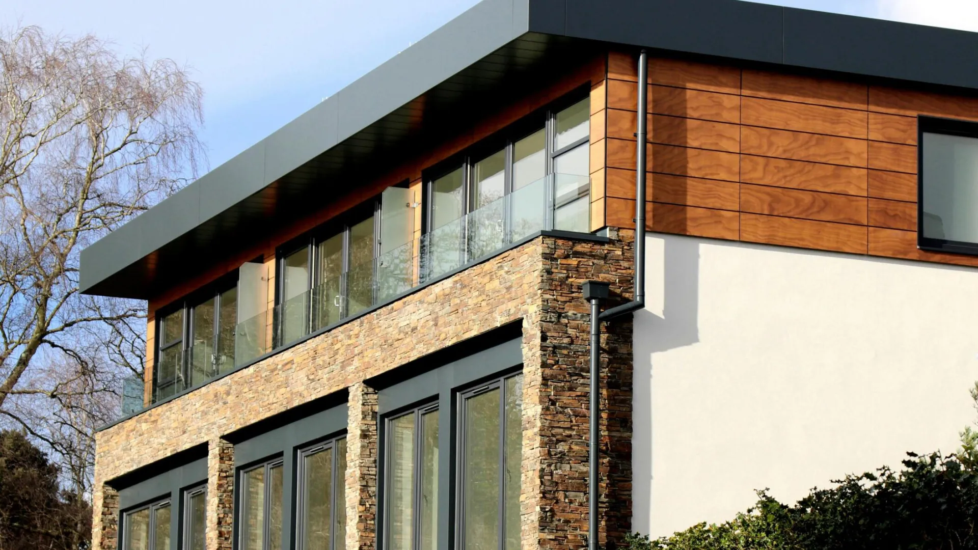 Contemporary house in Poole featuring a striking mix of stone and wood facade with large windows.