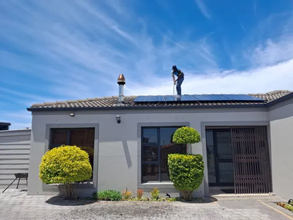 A worker installs solar panels on a house roof under a clear blue sky, showcasing renewable energy adoption.