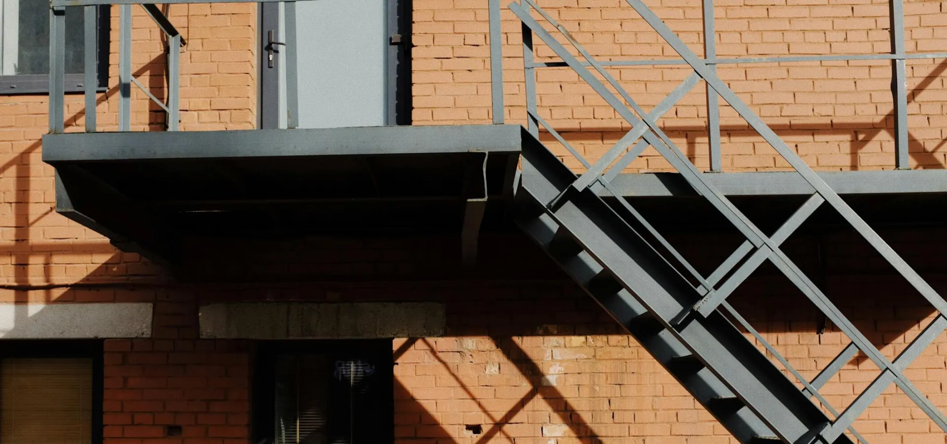 A contemporary brick building facade with metal stairs in daylight, casting intricate shadows outdoors.