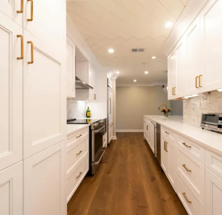 Bright modern kitchen with white cabinets, wooden floor, and appliances.